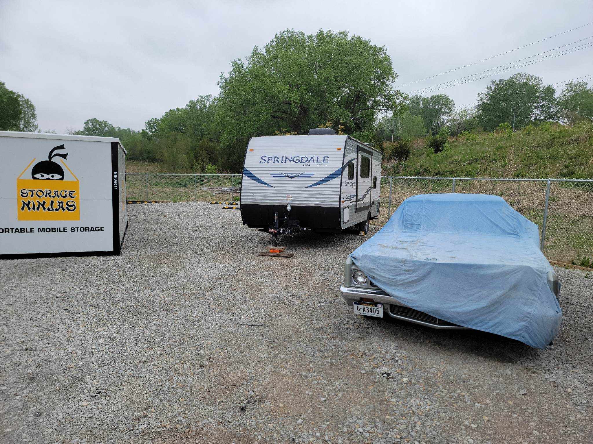 A Storage Ninjas Portable Container near a parked RV and covered car on gravel.